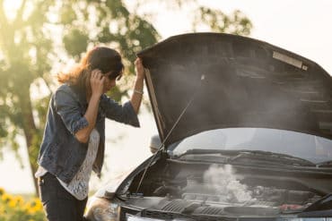 sad woman standing on the road by the broken car