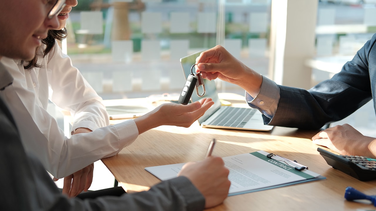 dealer salesman giving car key to new owner. client signing insurance document or rental car lease form