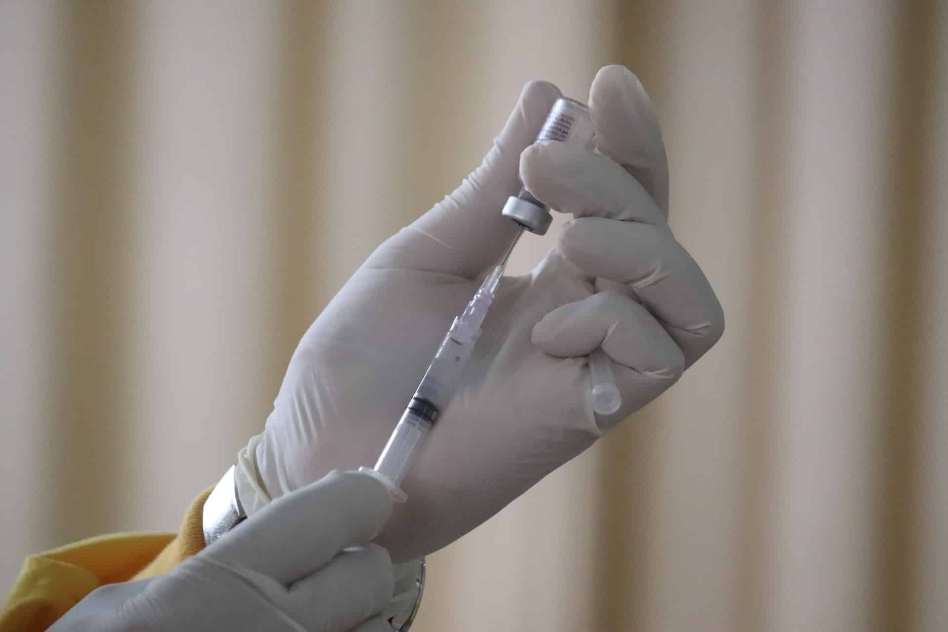 a gloved hand draws fluid out of a covid vaccine bottle using a syringe