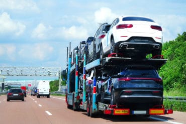 Sherpa Auto Transport reviews mention easy shipping with transport options like this open car carrier with multiple vehicles traveling down a highway.